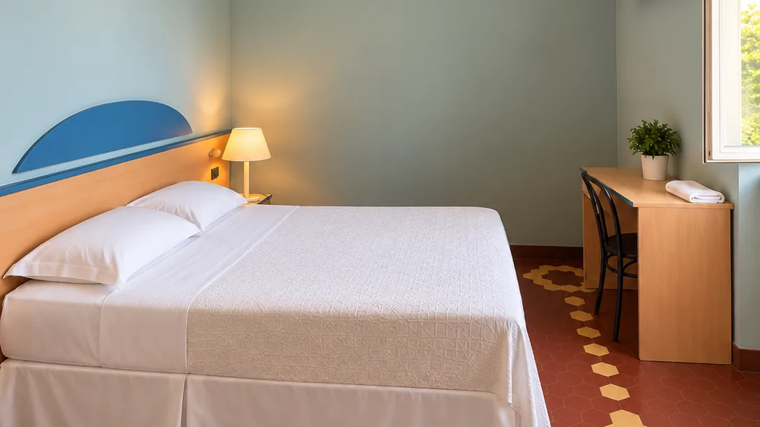 Bedroom with double bed, blue and wood headboard, bedside lamp, desk and pale green walls - Hotel Rex, BZAR hotels in Lucca
