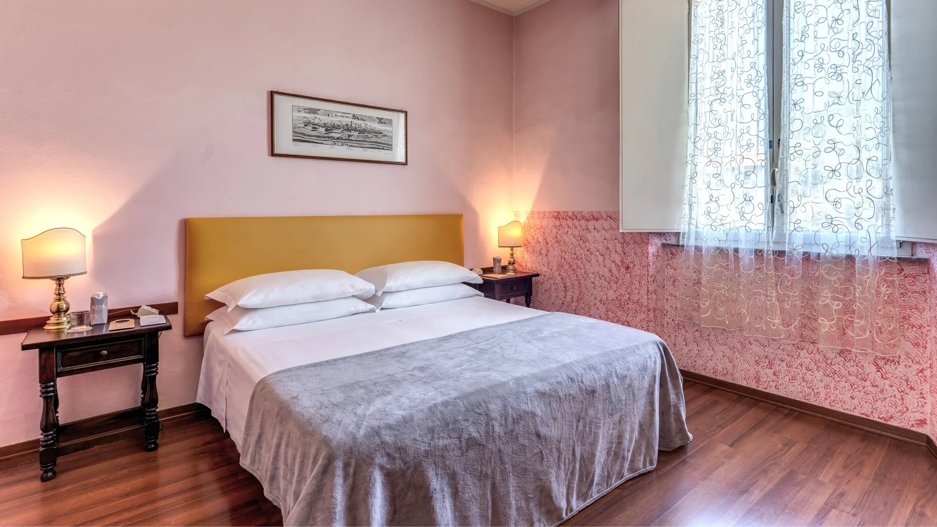 Double room with large bed, pink walls, mustard headboard, vintage bedside tables and bright window - Hotel Rex, BZAR hotels in Lucca