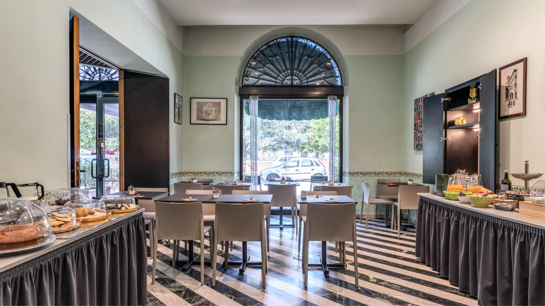 Bright breakfast room with buffet, set tables, large arched window and view of the Lucca area - Hotel Rex, BZAR hotels in Lucca