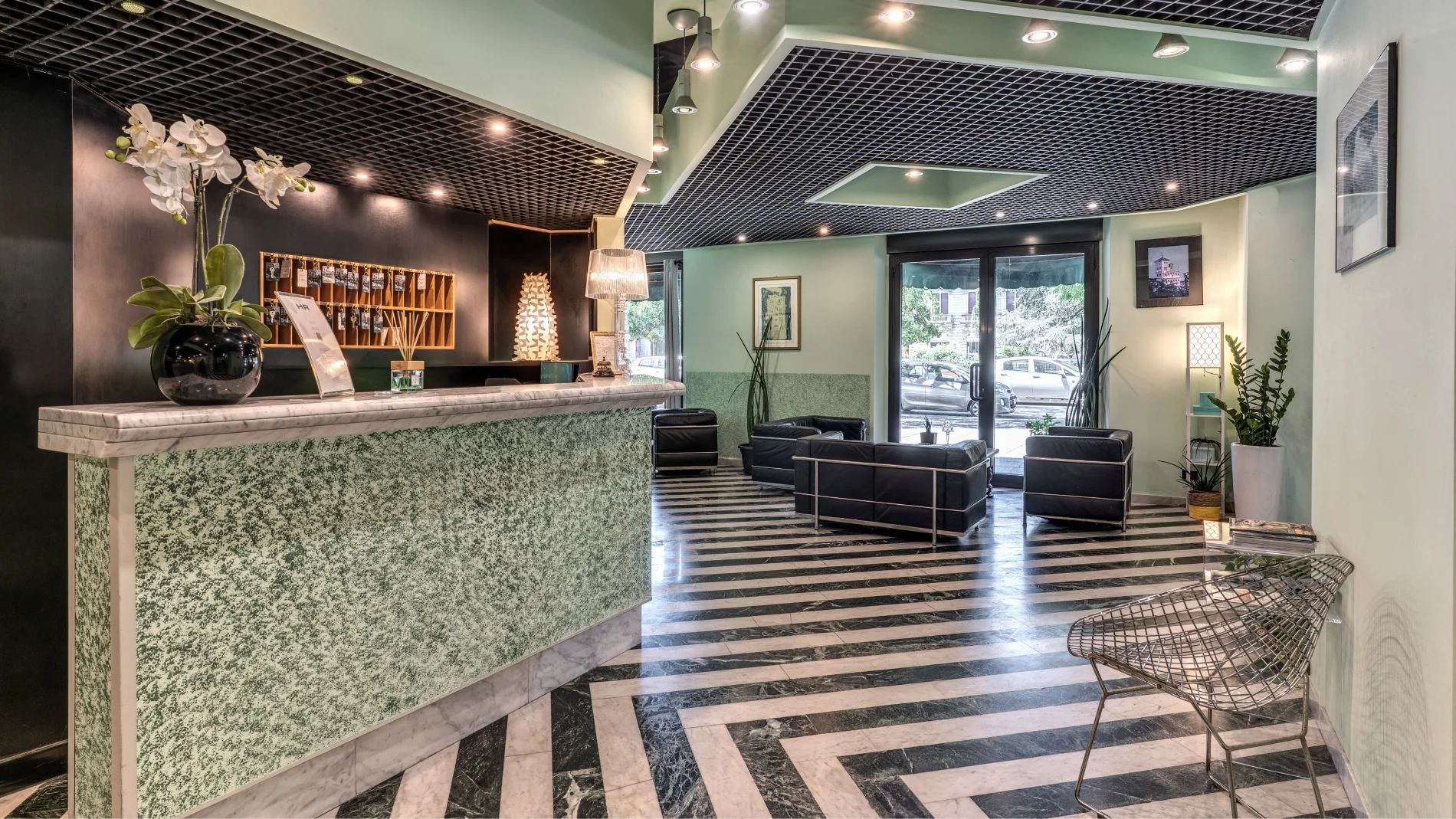 Reception with marble desk, striped floor, lounge area with black armchairs and street-facing windows - Hotel Rex, BZAR hotels in Lucca