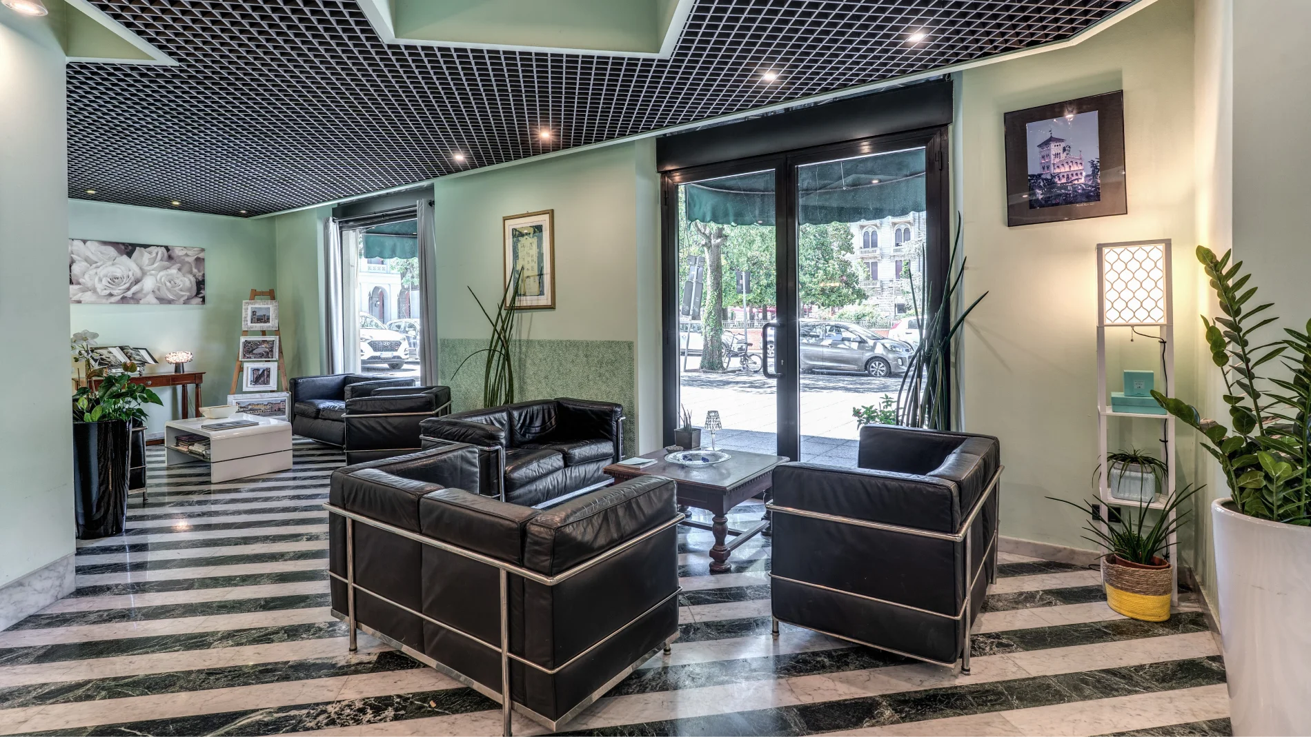 Welcoming lobby with black leather armchairs, central coffee table, decorative plants and large windows - Hotel Rex, BZAR hotels in Lucca