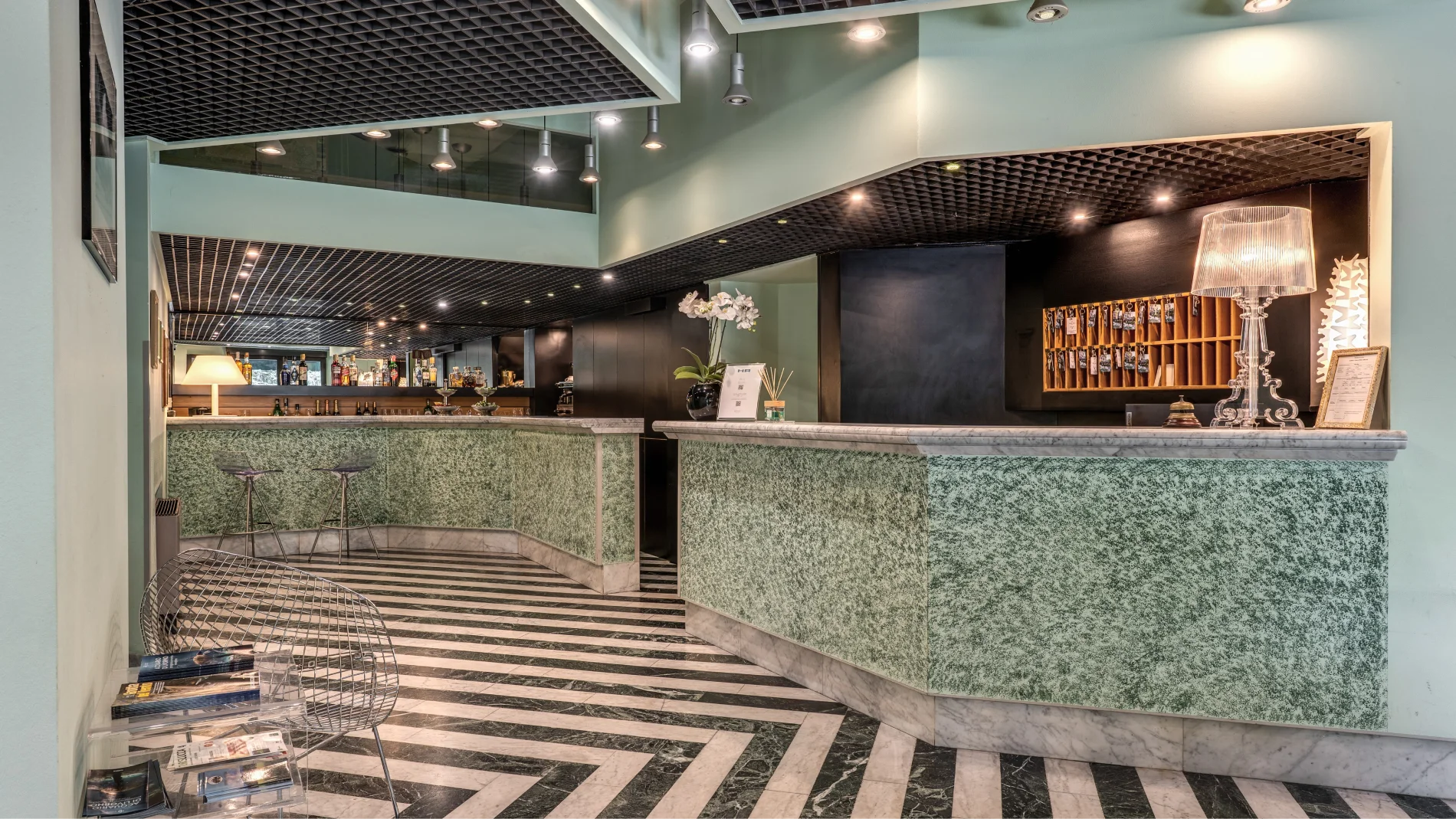 Bar and reception counter with marble top, key shelf, decorative lamp and sage green finishes - Hotel Rex, BZAR hotels in Lucca