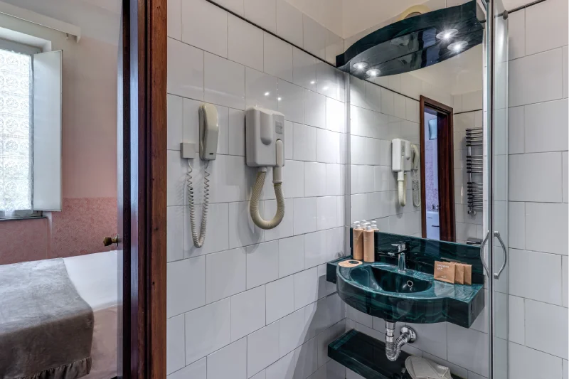 Bathroom detail with glossy black sink, mirror, amenities, glass shower and white tiles - Hotel Rex, BZAR hotels in Lucca