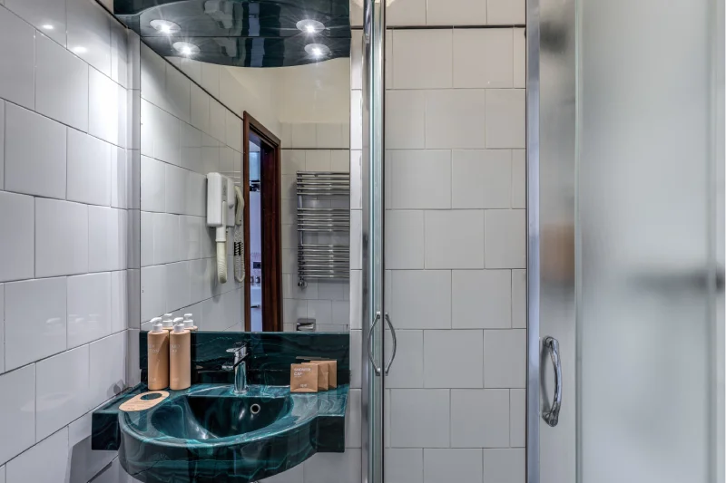 Private bathroom with modern glass shower, black sink, illuminated mirror and courtesy set - Hotel Rex, BZAR hotels in Lucca