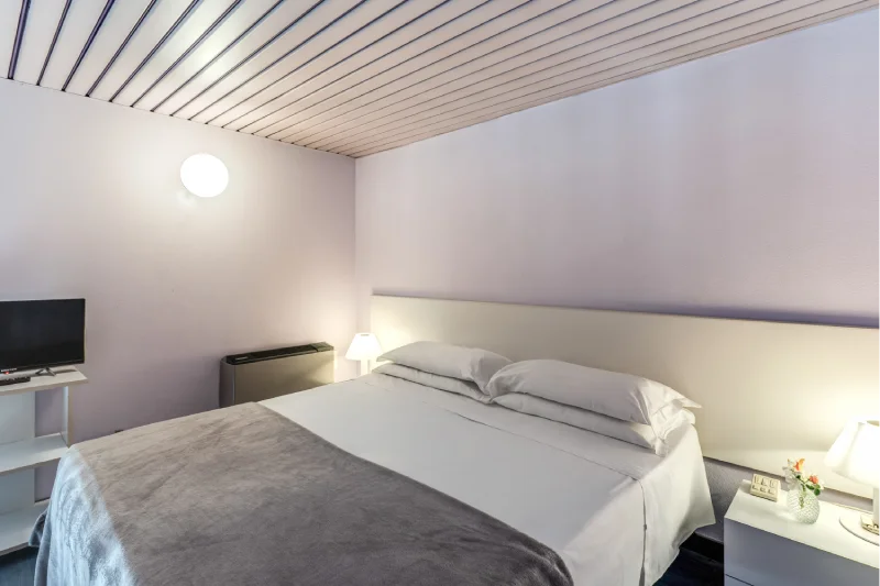 Split-level family room with double bed, slatted ceiling, TV, white bedside tables and warm lights - Hotel Rex, BZAR hotels in Lucca