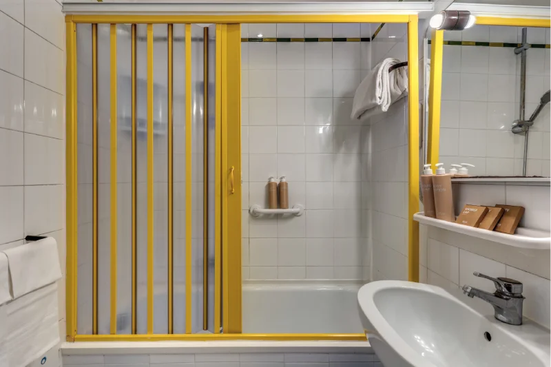 Family bathroom with shower bath, yellow screen, white sink, illuminated mirror and courtesy set - Hotel Rex, BZAR hotels in Lucca