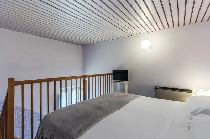 Mezzanine sleeping area with double bed, wooden railing, TV, lilac walls and soft lighting - Hotel Rex, BZAR hotels in Lucca