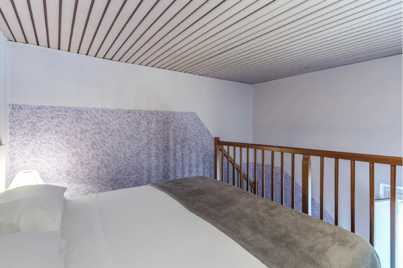 Double bed on mezzanine with wooden railing, slatted ceiling and decorated lilac walls - Hotel Rex, BZAR hotels in Lucca
