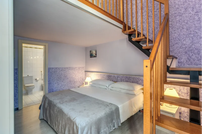 Family room with double bed, internal wooden staircase, private bathroom and decorated lilac walls - Hotel Rex, BZAR hotels in Lucca