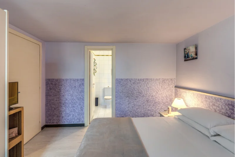 Lower-level family room with double bed, TV, wardrobe, bathroom entrance and bedside lights - Hotel Rex, BZAR hotels in Lucca