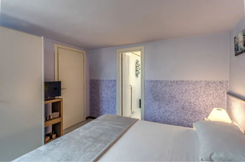 Family room with double bed, bathroom door, TV on cabinet, light wardrobe and lilac walls - Hotel Rex, BZAR hotels in Lucca
