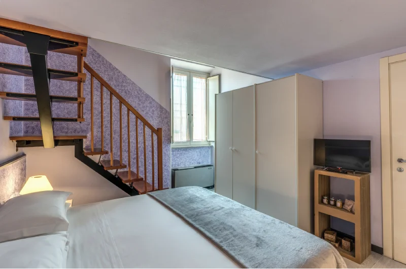 Family room with double bed, mezzanine staircase, wardrobe, TV, tall window and natural light - Hotel Rex, BZAR hotels in Lucca