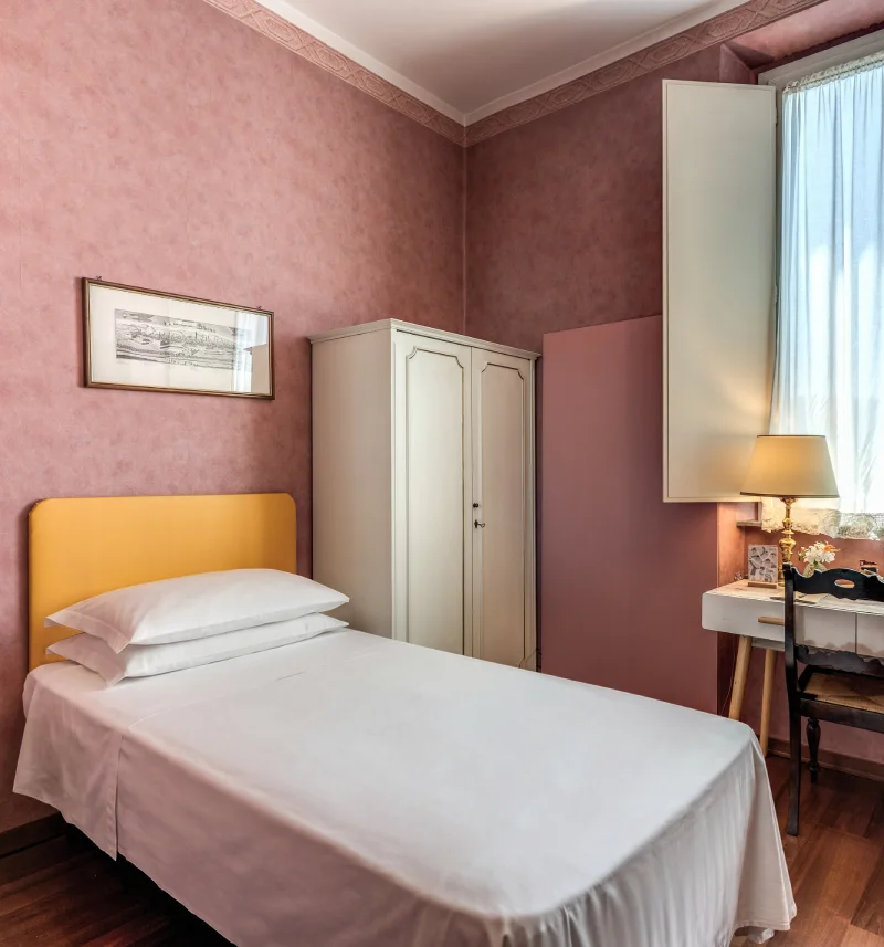 Cozy single room with bed, light wardrobe, desk, pink walls and wooden floor - Hotel Rex, BZAR hotels in Lucca