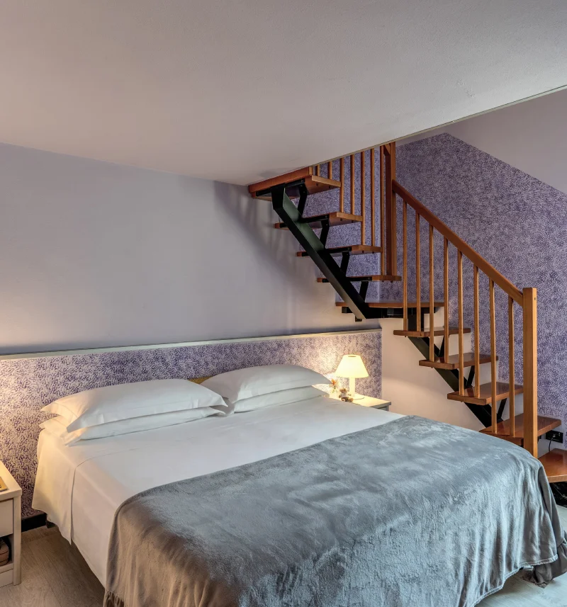 Split-level room with double bed, wooden internal staircase, lilac walls and warm lighting - Hotel Rex, BZAR hotels in Lucca