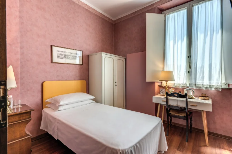 Bright single room with bed, mustard headboard, light wardrobe, desk and tall window - Hotel Rex, BZAR hotels in Lucca