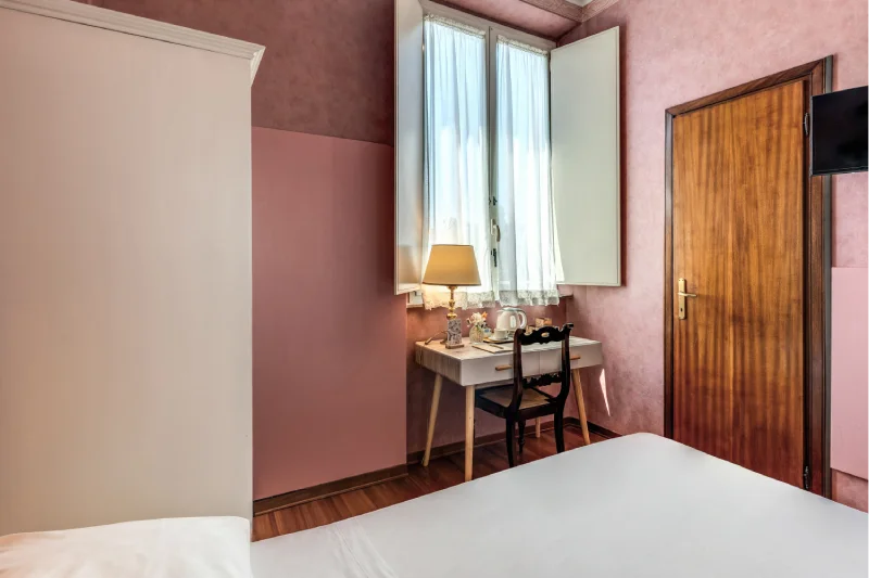 Single room with desk corner, window with light curtains, wooden door and warm flooring - Hotel Rex, BZAR hotels in Lucca
