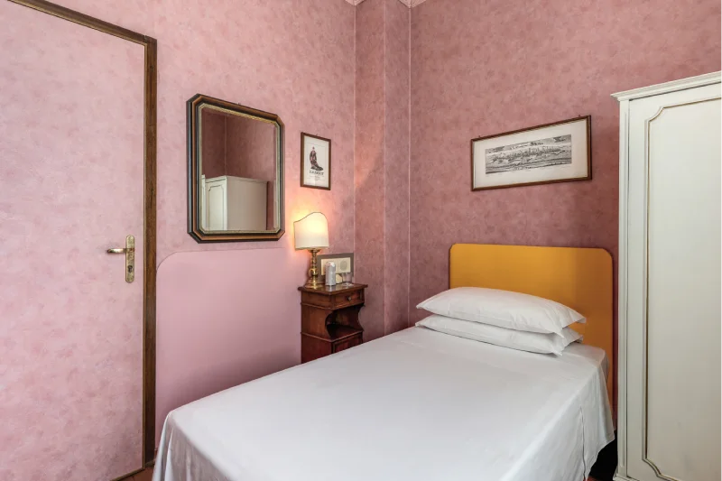 Classic single room with bed, mustard headboard, mirror, vintage bedside table and light wardrobe - Hotel Rex, BZAR hotels in Lucca