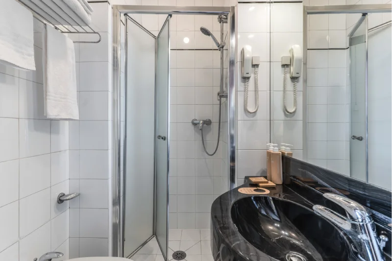 Private bathroom with glass shower, black sink, mirror, towels and white wall tiles - Hotel Rex, BZAR hotels in Lucca