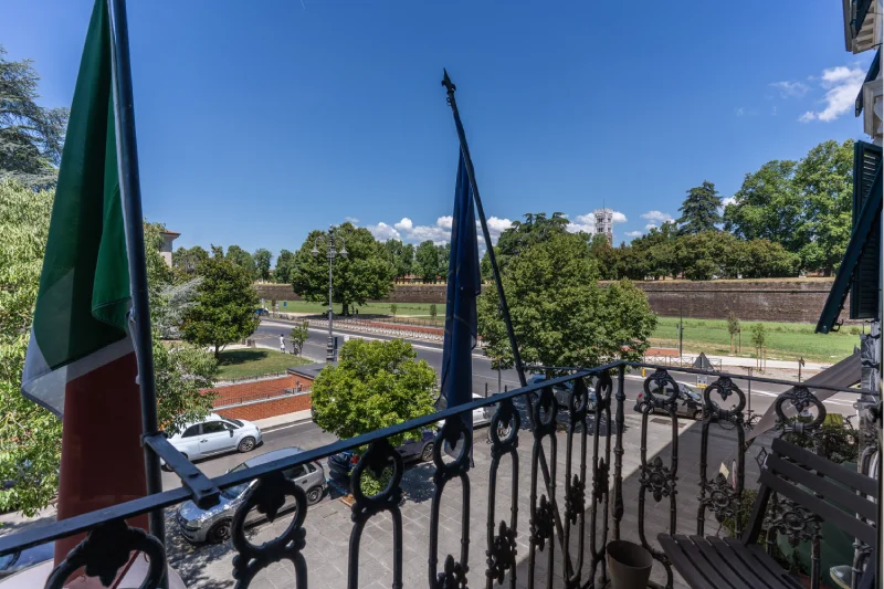 View from the suite balcony with flags, iron railing, trees and the historic walls of Lucca - Hotel Rex, BZAR hotels in Lucca