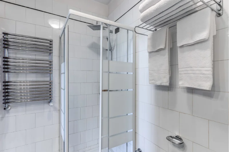 Suite bathroom detail with glass shower enclosure, chrome towel warmer, towels and white tiles - Hotel Rex, BZAR hotels in Lucca