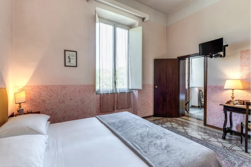 Suite with double bed, tall window, wall-mounted TV, vintage desk and decorated pink walls - Hotel Rex, BZAR hotels in Lucca