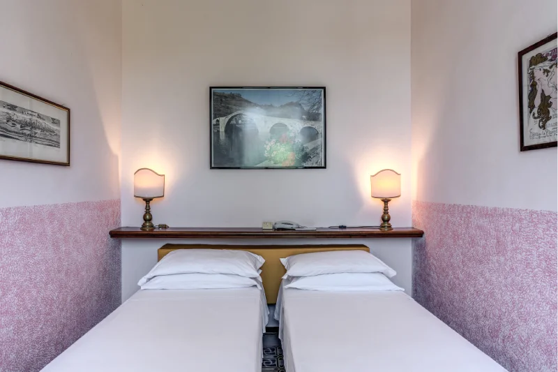 Twin suite with two single beds, mustard headboard, lit lamps, decorative artwork and pink walls - Hotel Rex, BZAR hotels in Lucca