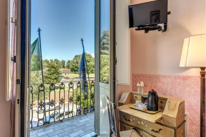 Suite with balcony overlooking greenery, flags, iron railing, wall-mounted TV and tea corner - Hotel Rex, BZAR hotels in Lucca