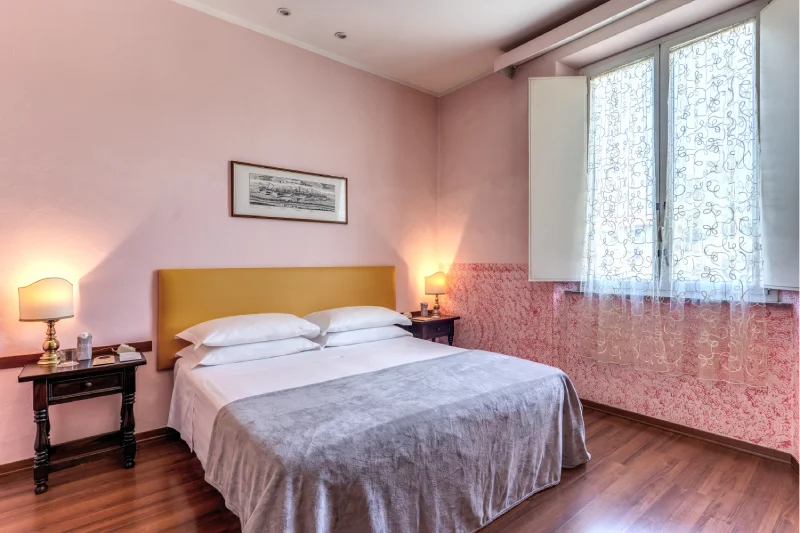 Double bed in triple room with mustard headboard, classic bedside tables, tall window and parquet floor - Hotel Rex, BZAR hotels in Lucca