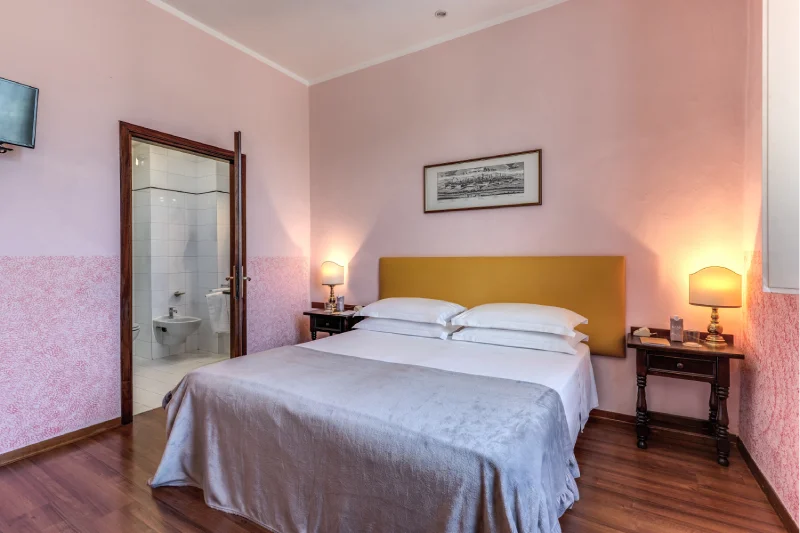 Triple room with double bed, visible private bathroom, pink walls, bedside tables and wall-mounted TV - Hotel Rex, BZAR hotels in Lucca