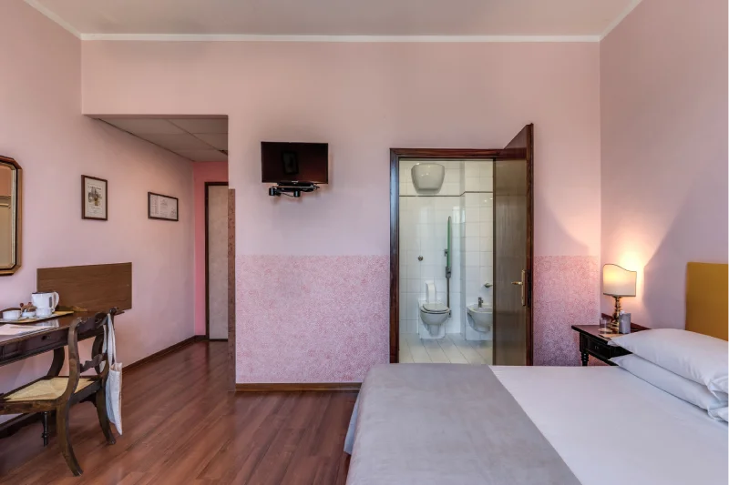 Triple room with double bed, desk, wall-mounted TV, bathroom door and warm lighting - Hotel Rex, BZAR hotels in Lucca