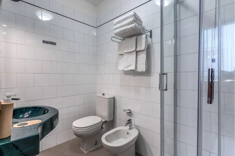 Private bathroom with glass shower, dark green sink, toilet, bidet and white towels - Hotel Rex, BZAR hotels in Lucca
